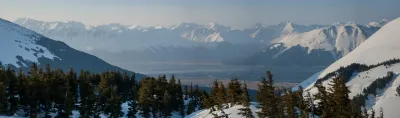 A high-altitude panoramic view looking down into a broad, snow-filled valley surrounded by jagged, snow-covered mountains.