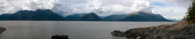 A wide panoramic view of Turnagain Arm from Hope, Alaska, showing the dark green mountains and dramatic, cloudy sky.