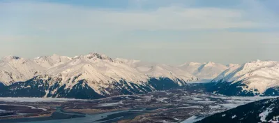 Another wide panoramic view of the snow-covered Alaskan landscape, featuring a vast valley and river surrounded by mountains.