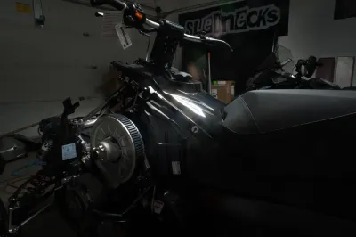 A close-up of the internal engine and belt system of a snowmobile in a garage, with a 'SLEDNECKS' banner in the background.