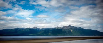 A wide panoramic view of Turnagain Arm in Alaska, with dark green mountains and a dramatic, cloudy sky.