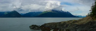 A wide panoramic view of Turnagain Arm and the surrounding mountains in Alaska under a dramatic sky.