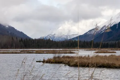 A wide-angle view of a vast marshy or wetland area with multiple small ponds, set against a backdrop of snow-capped mountains.