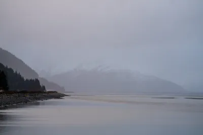A moody, overcast shot of Turnagain Arm at low tide, with mountains silhouetted against the grey sky.