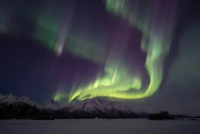 A swirling green and purple aurora crown over a broad, snowy mountain landscape.