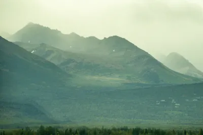 A lush, green Alaskan mountain range under a heavy, low-lying mist or fog.