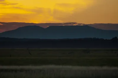 A stunning sunset over a silhouetted Alaskan mountain range, with vibrant orange and yellow light filling the sky.