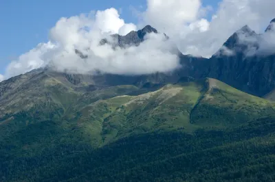 A close-up view of jagged, green mountains in Alaska partially shrouded by white clouds.