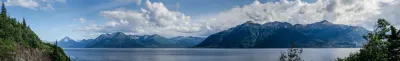 A wide panoramic view of the Kenai Mountains and Kachemak Bay at low tide, with dramatic clouds and patches of blue sky.