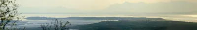 A hazy, wide panoramic view from Anchorage looking over the mudflats of Cook Inlet towards distant mountains.
