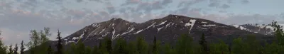 A wide panoramic shot of snow-dusted Alaskan mountains under a soft pink and grey twilight sky.