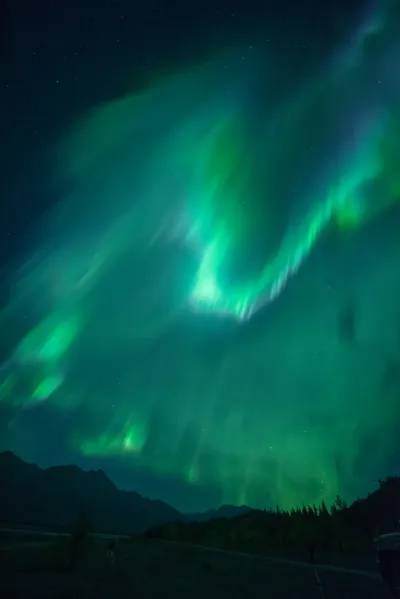 A broad, swirling green aurora crown dominates the dark night sky over a mountain range.