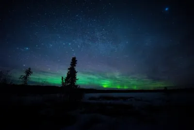 A vast, starry sky with a faint green aurora band hanging over a dark, silhouetted landscape.