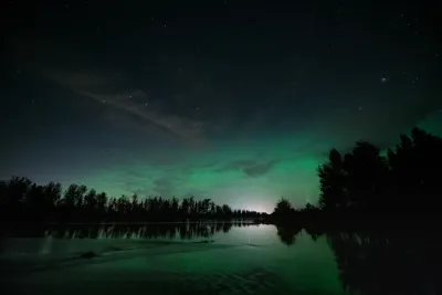 A wide-angle view of a clear starry night with a soft green aurora glow low on the horizon, reflected in a river.