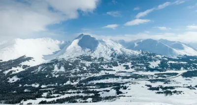 A vast, snow-covered Alaskan valley surrounded by majestic mountain peaks under a clear blue sky.