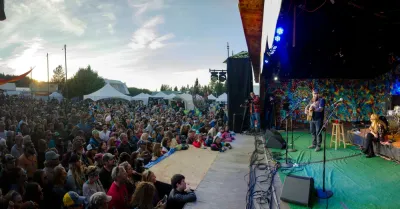 A wide-angle view of a live outdoor music performance in Alaska, with a large crowd gathered in front of a stage.
