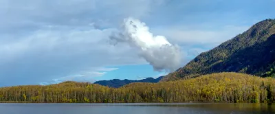 A vertical panoramic view of a calm lake reflecting a lush green hillside and a dramatic white cloud in the sky.