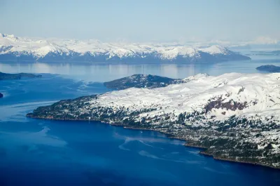A high-altitude view of snow-dusted islands and mountains in the blue waters of Kachemak Bay, Alaska.