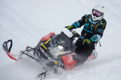 A high-action shot of a snowmobiler carving into deep snow.