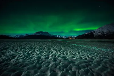 A wide field view of a frozen landscape with a soft, patterned green aurora glow in the starry sky.
