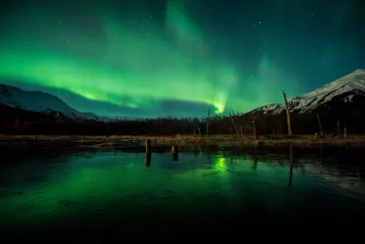 A reflection shot of a bright green aurora in the lake, with beautiful vertical structures in the light curtains.