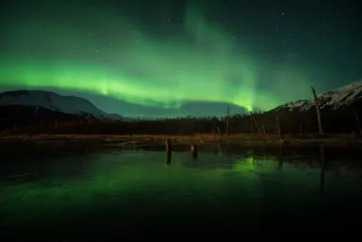 A wider view showing the broad arc of a green aurora reflected across a frozen body of water.