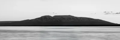 A long black and white panoramic view of Mount Susitna (Sleeping Lady) across the calm waters of Cook Inlet.