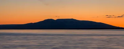 A wide color panoramic view of the Sleeping Lady (Mount Susitna) during a vibrant orange and pink sunset.